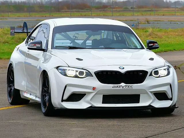 white bmw m240i racecar driving on the road with grass in the background