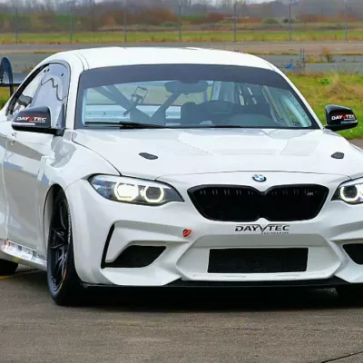 white bmw m240i racecar driving on the road with grass in the background