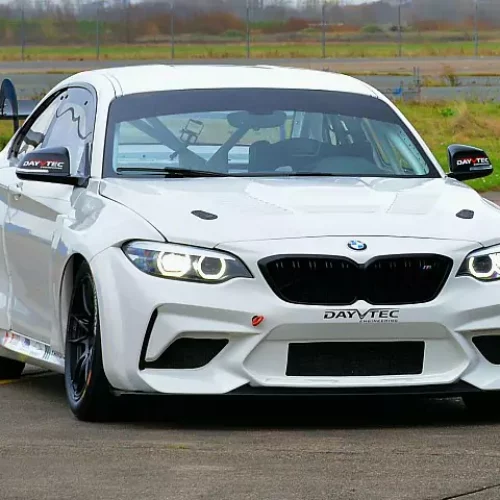 white bmw m240i racecar driving on the road with grass in the background